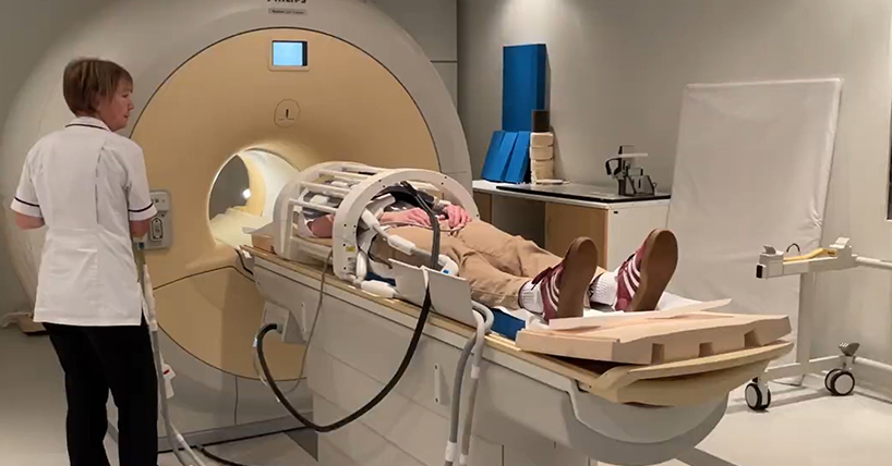 A radiographer helps a patient lying down about to enter an MRI scanner